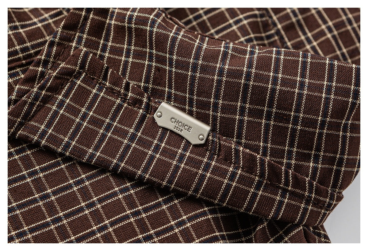 Close-up of a small metal badge on brown plaid fabric.