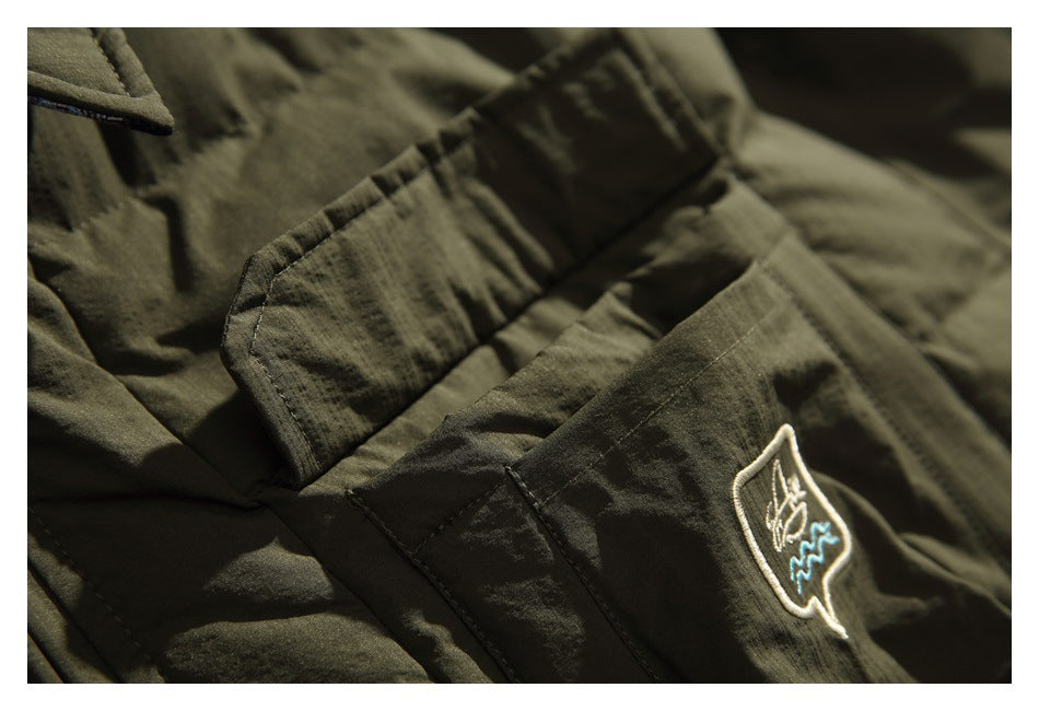 Close-up of an olive jacket pocket with a small embroidered emblem and stitched flap details.