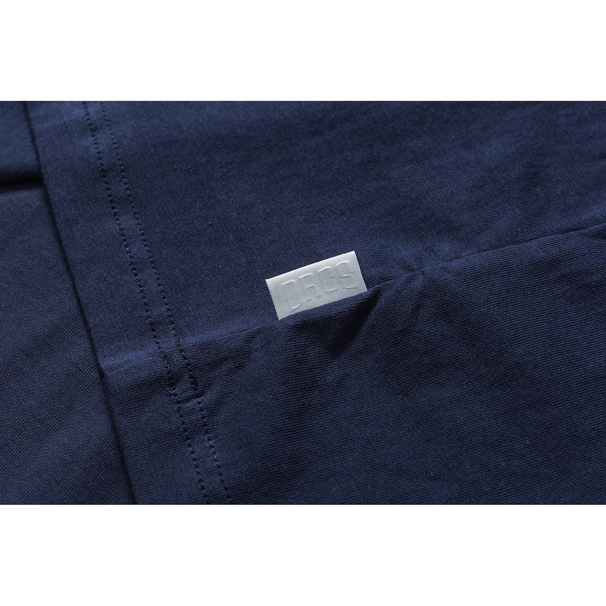 Close-up of navy shirt fabric, a seam, and a small white embossed fabric tab.