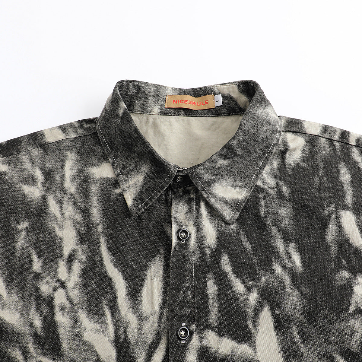 Close-up of a black and cream abstract-patterned shirt collar, button placket, and sewn neck label.