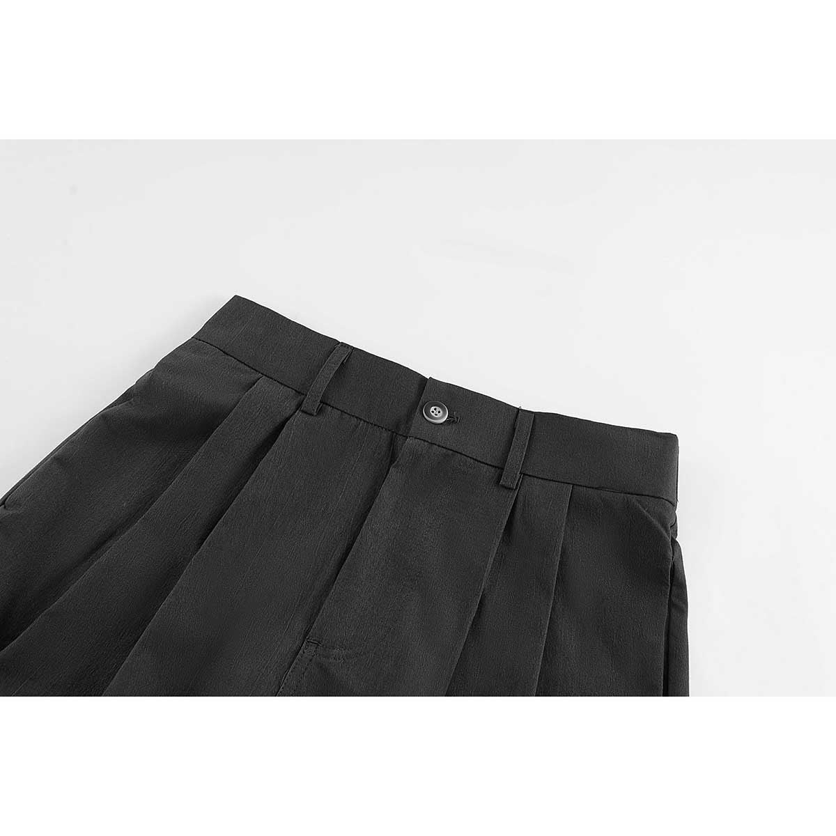 Close-up of black shorts showing the buttoned waistband, belt loops, front pleats and side pockets.