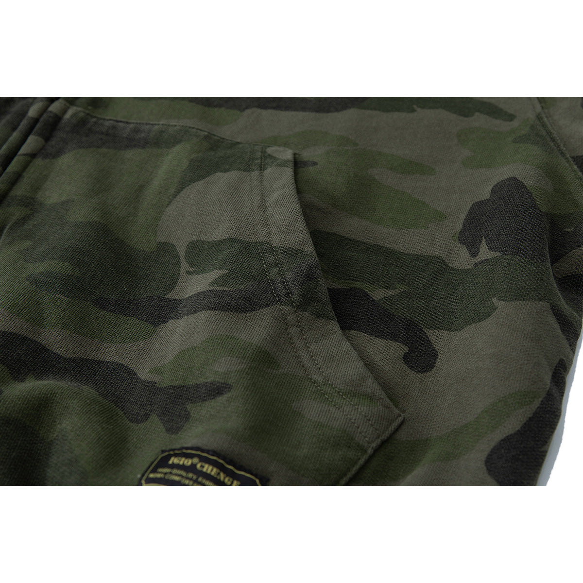 Close-up of a dark green camouflage hoodie pocket and stitching, with a small sewn patch near the hem.