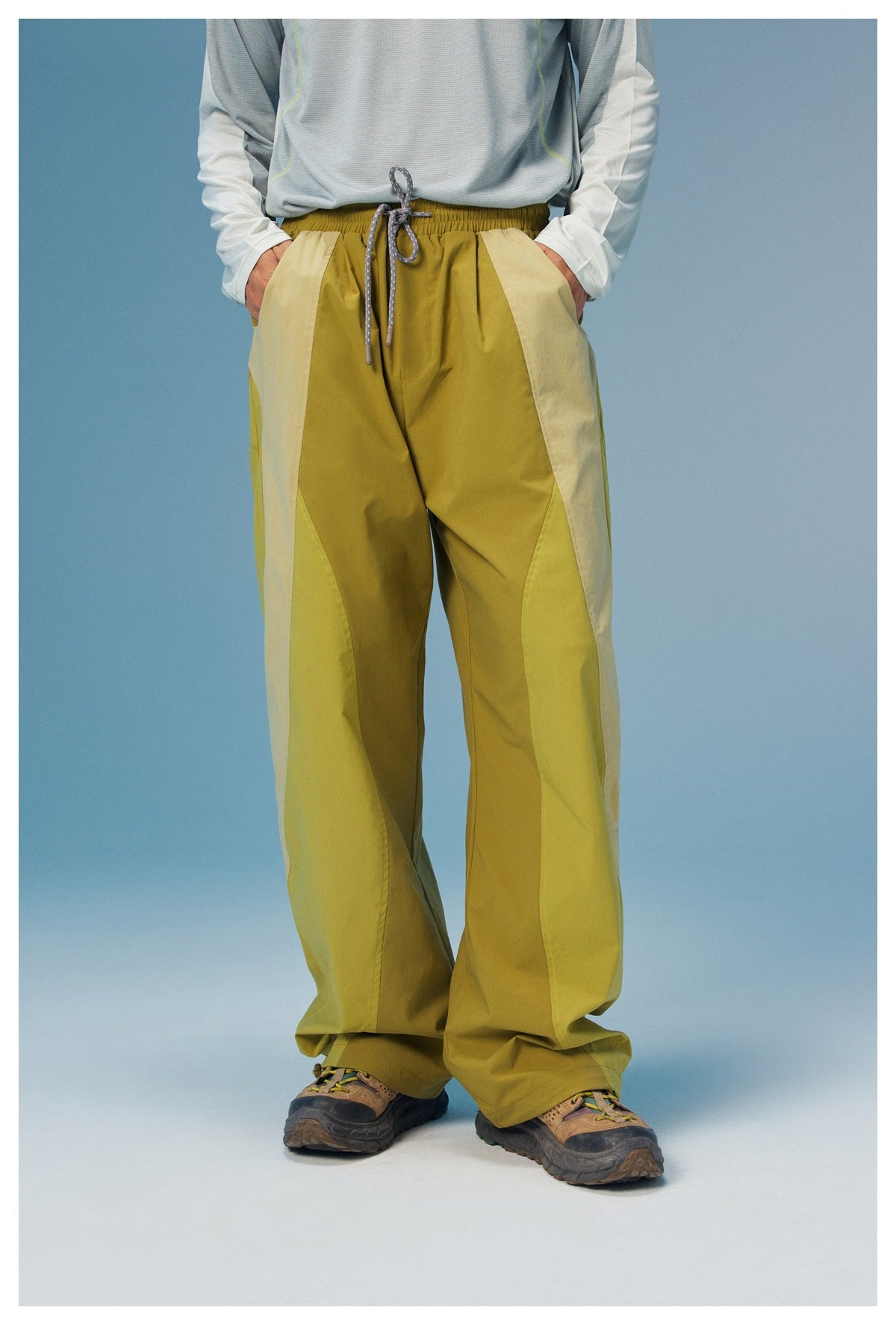 Front view of a model wearing loose olive trousers with pale side panels, an elastic drawstring waist and side pockets.