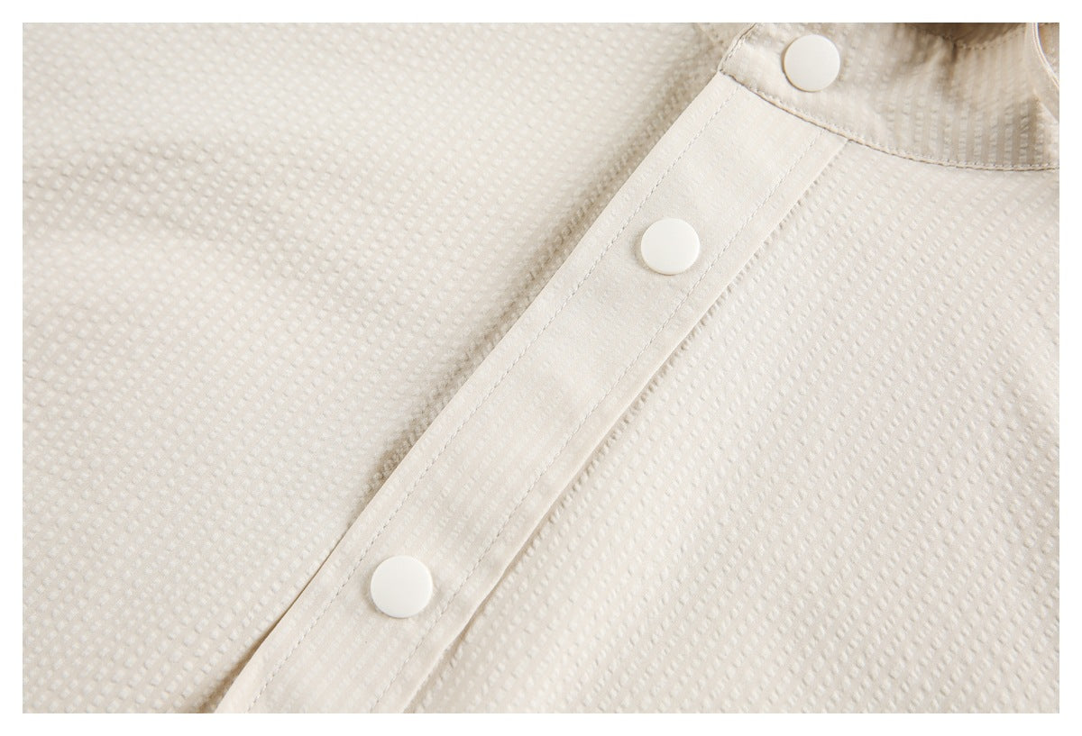 Close-up of two white snaps on the placket of a cream textured garment.