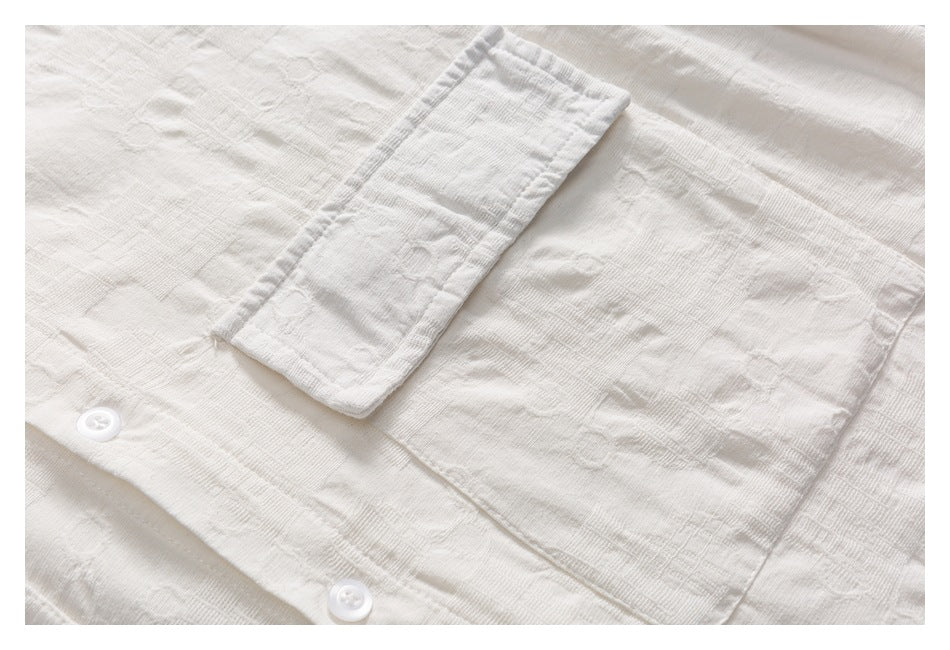 Close-up of a white shirt’s textured fabric, front buttons, and rectangular chest pocket.