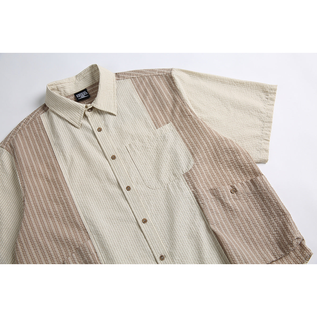 Close view of a beige short-sleeve button-up shirt with a chest pocket and contrasting brown striped panels.