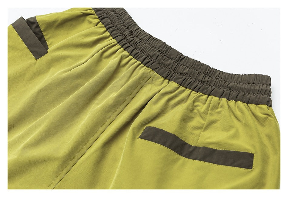 Close-up of yellow-green shorts showing a dark elastic waistband and dark-trimmed pockets.