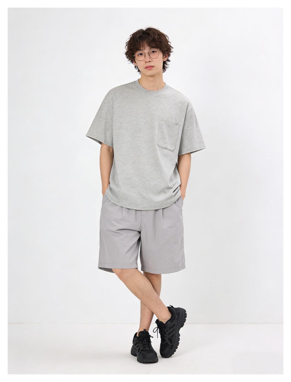 Front view of a model wearing a light gray pocket T-shirt, gray shorts, and black sneakers.