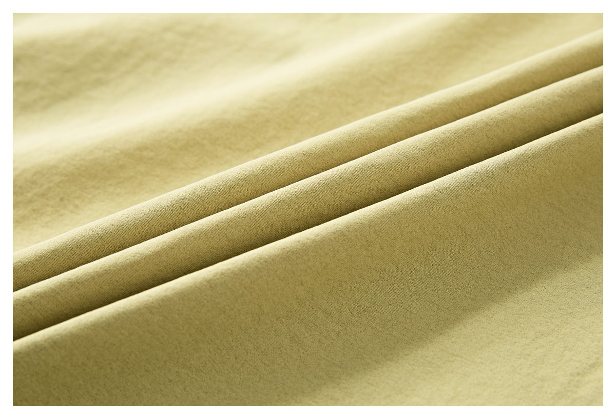 Close-up of pale olive-beige fabric draped in soft folds, showing its fine surface texture.