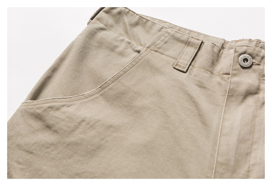 Close-up of beige trousers showing a curved front pocket, belt loop and metal waistband button.