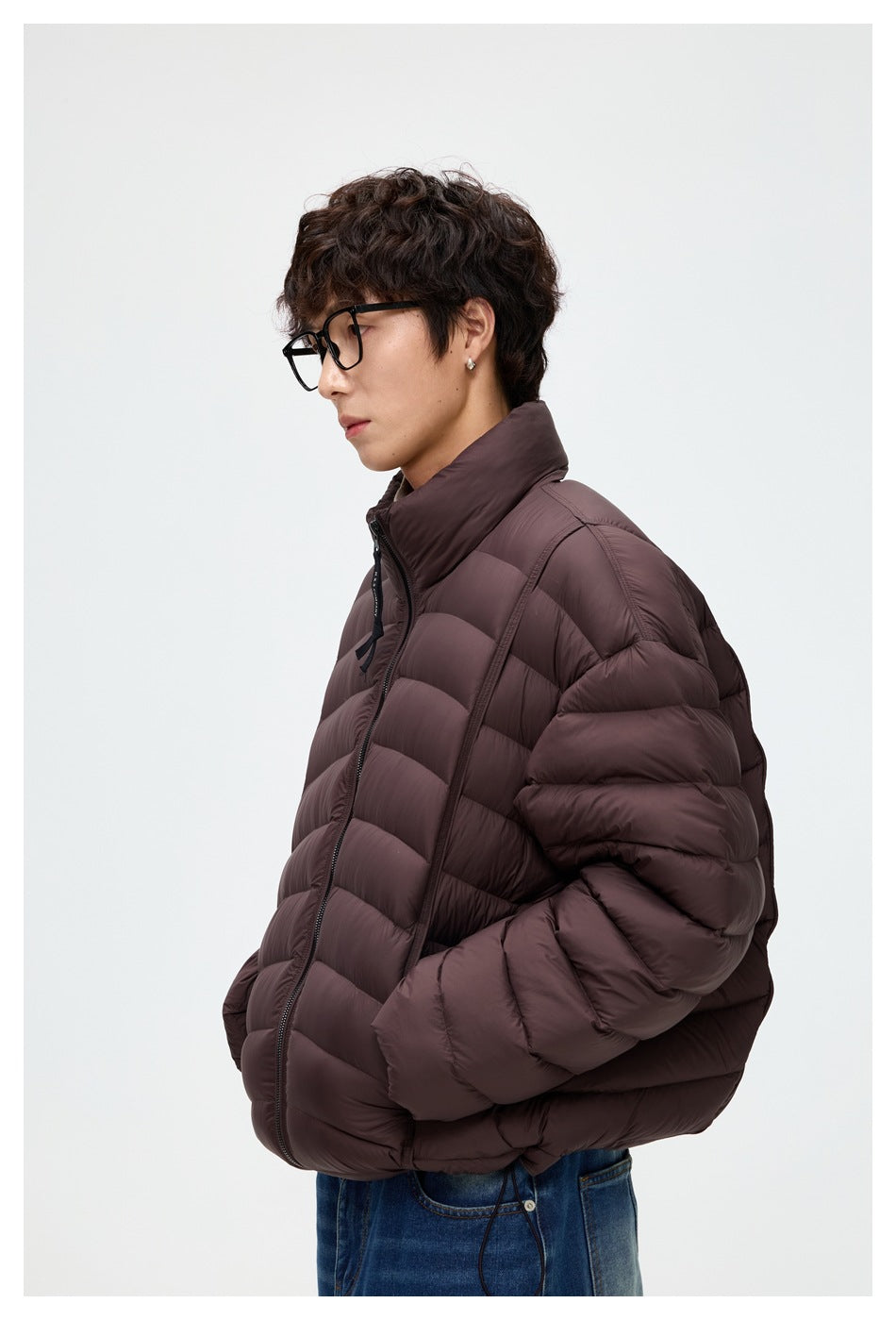Side view of a model wearing a dark plum-brown quilted puffer jacket with a high collar.