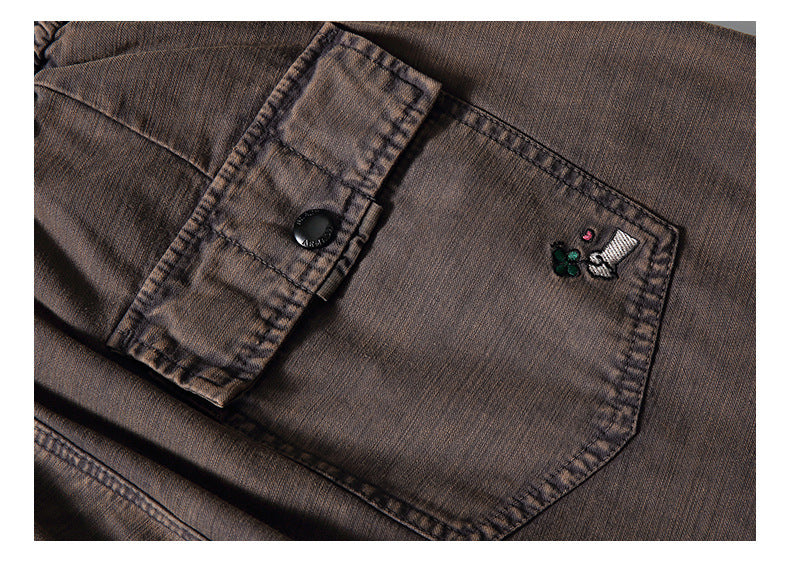 Close-up of a brown garment pocket with a flap, black button, and small embroidered motif.