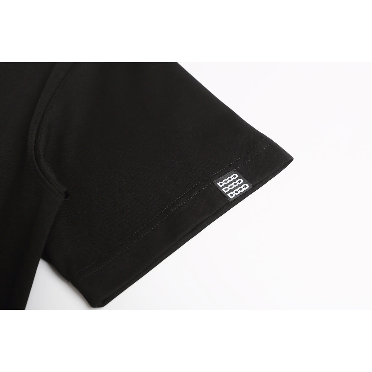 Close-up of a black T-shirt sleeve hem with a small black-and-white logo patch.