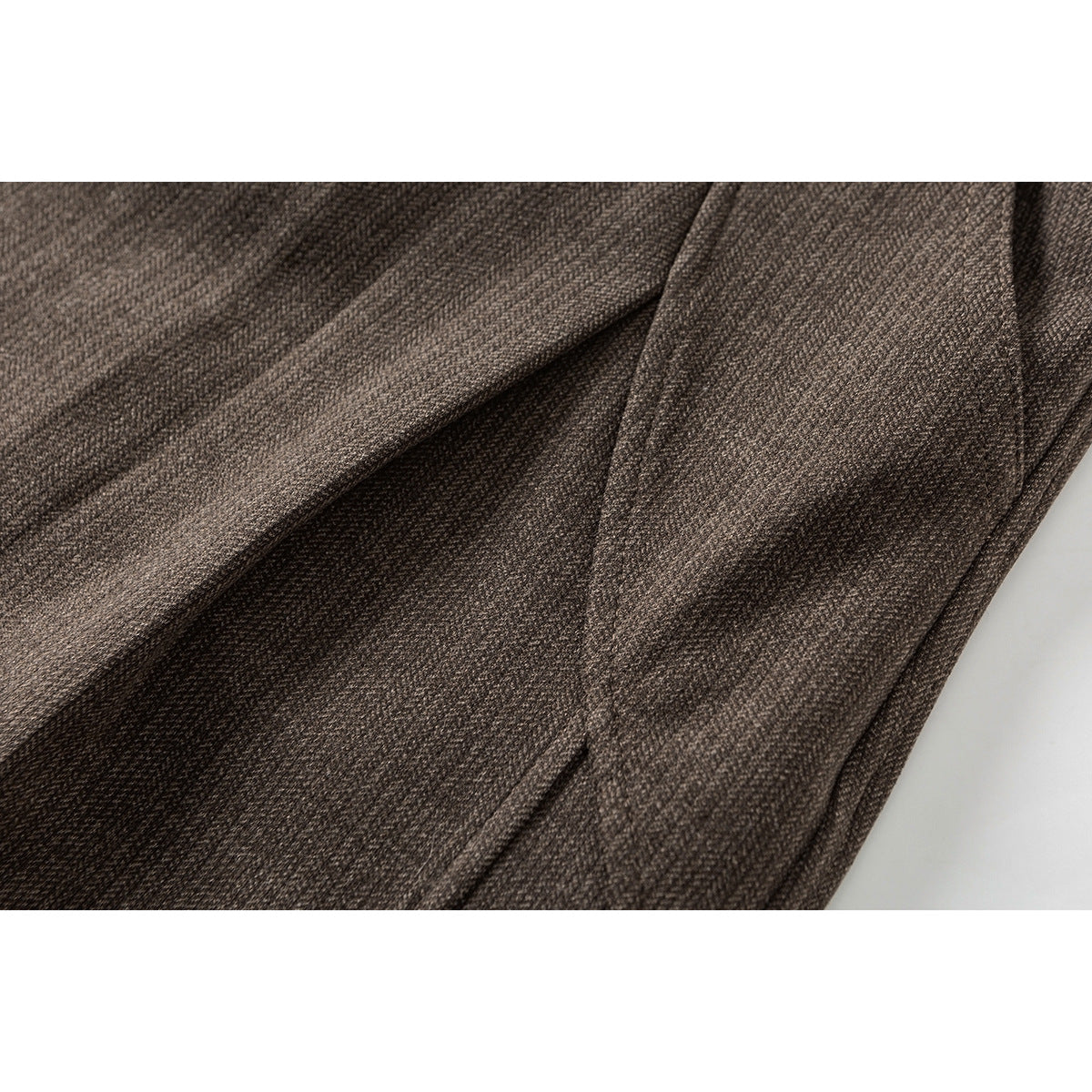 Close-up of the brown trousers' textured fabric and overlapping leg panels.