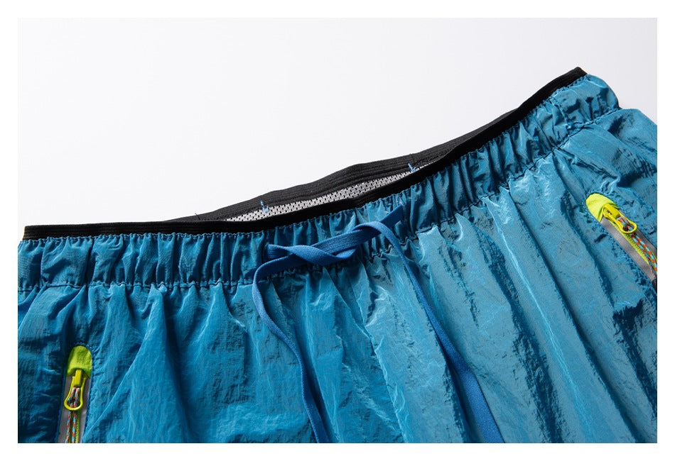 Close-up of teal-blue shorts showing the elastic waistband, drawcord, inner mesh lining, and neon-trimmed zip pocket.
