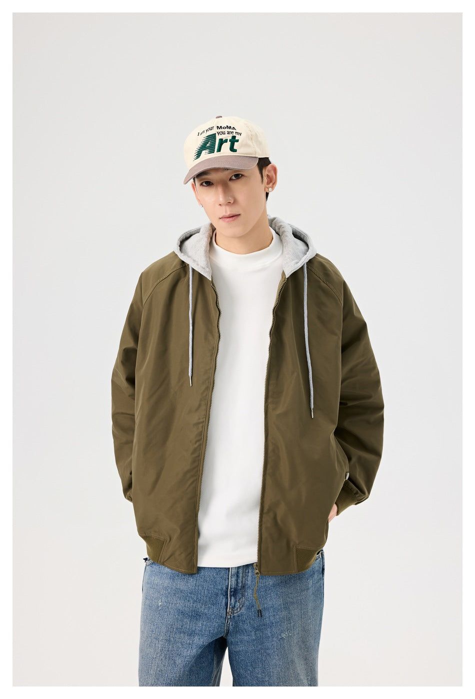 Close view of a model wearing an olive zip-front jacket with a gray hood and drawstrings.