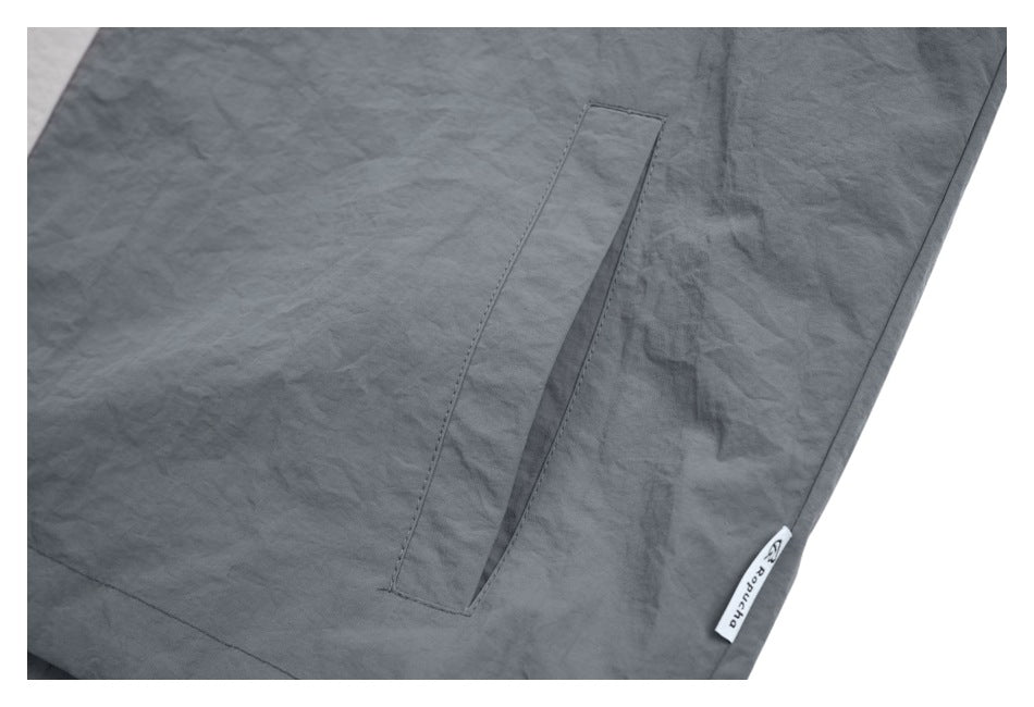 Close-up of a dark gray jacket’s narrow side pocket and small sewn side label.
