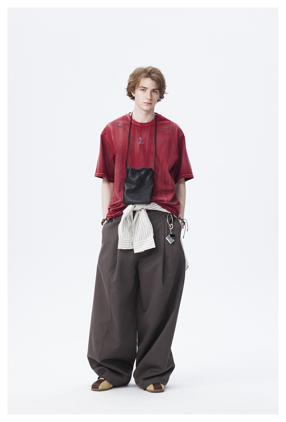Model wearing the red distressed T-shirt with wide brown trousers, black crossbody pouch and striped shirt at waist