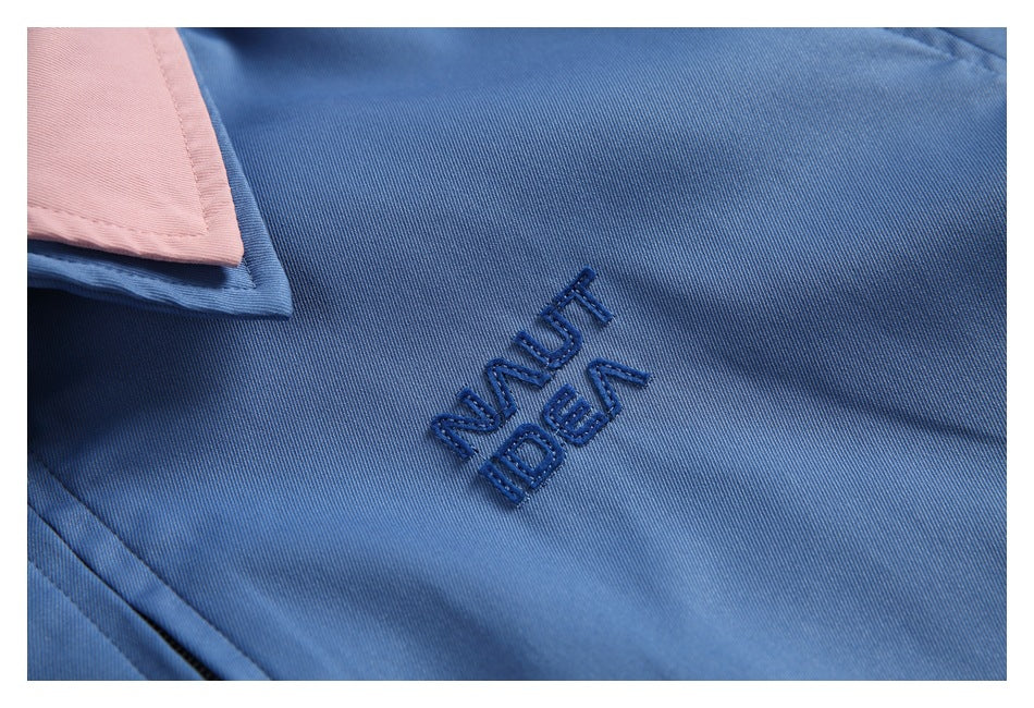 Close-up of dark blue embroidered lettering on blue fabric beside a pale pink collar.