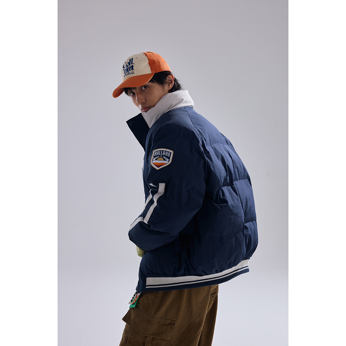 Model wearing a navy padded jacket with white sleeve stripes and a sleeve patch, shown from the side and back.