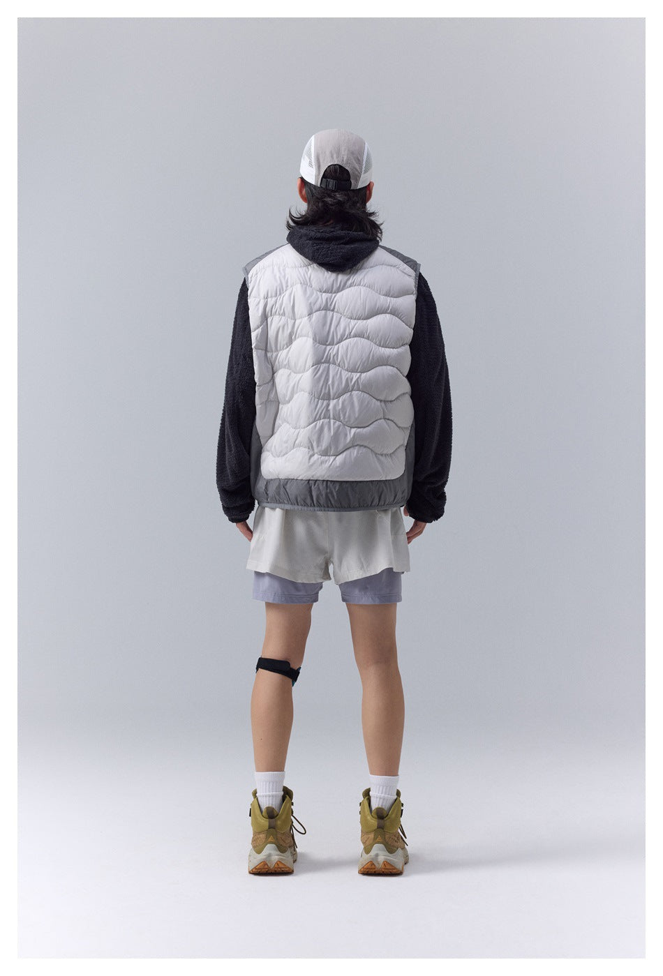 Back view of a hiker wearing a white quilted vest with gray shoulders and hem over a dark fleece hoodie.