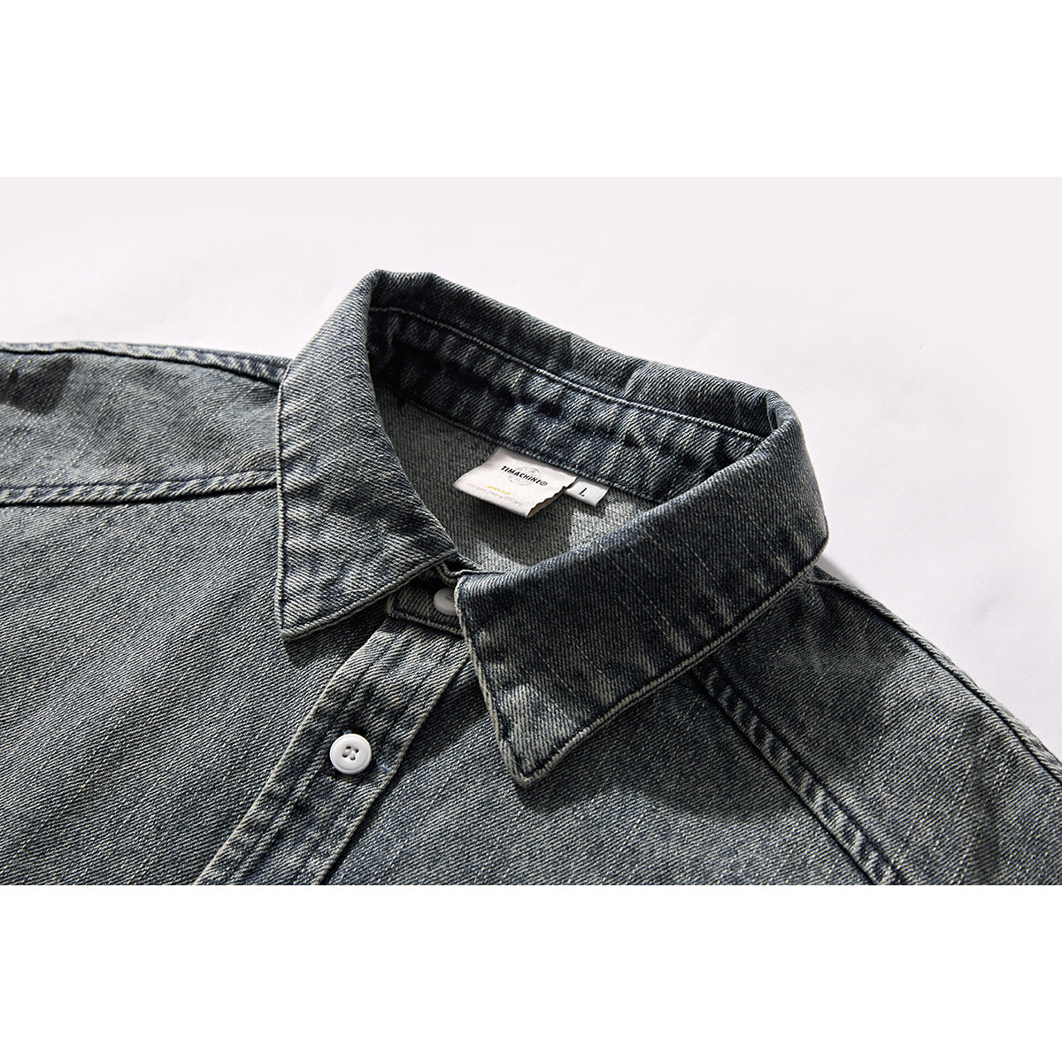 Close-up of a dark gray washed denim shirt collar, neckline, and white button.