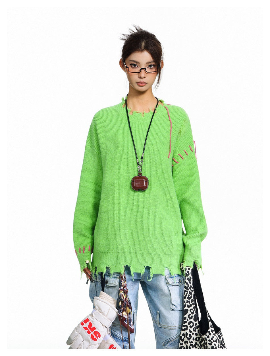 Model wearing green ribbed sweater with frayed neckline and pink stitching, styled with light-wash jeans and a pendant