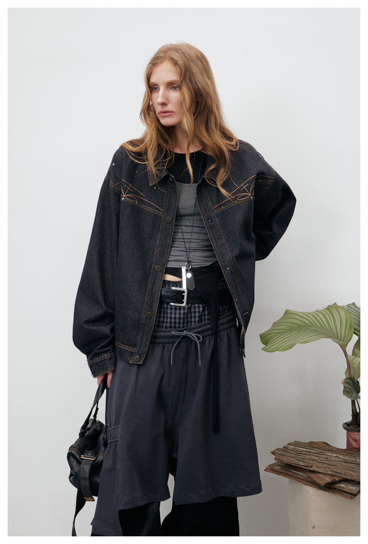 Model wearing an oversized black denim jacket with tan stitched motifs, paired with dark layered clothing.