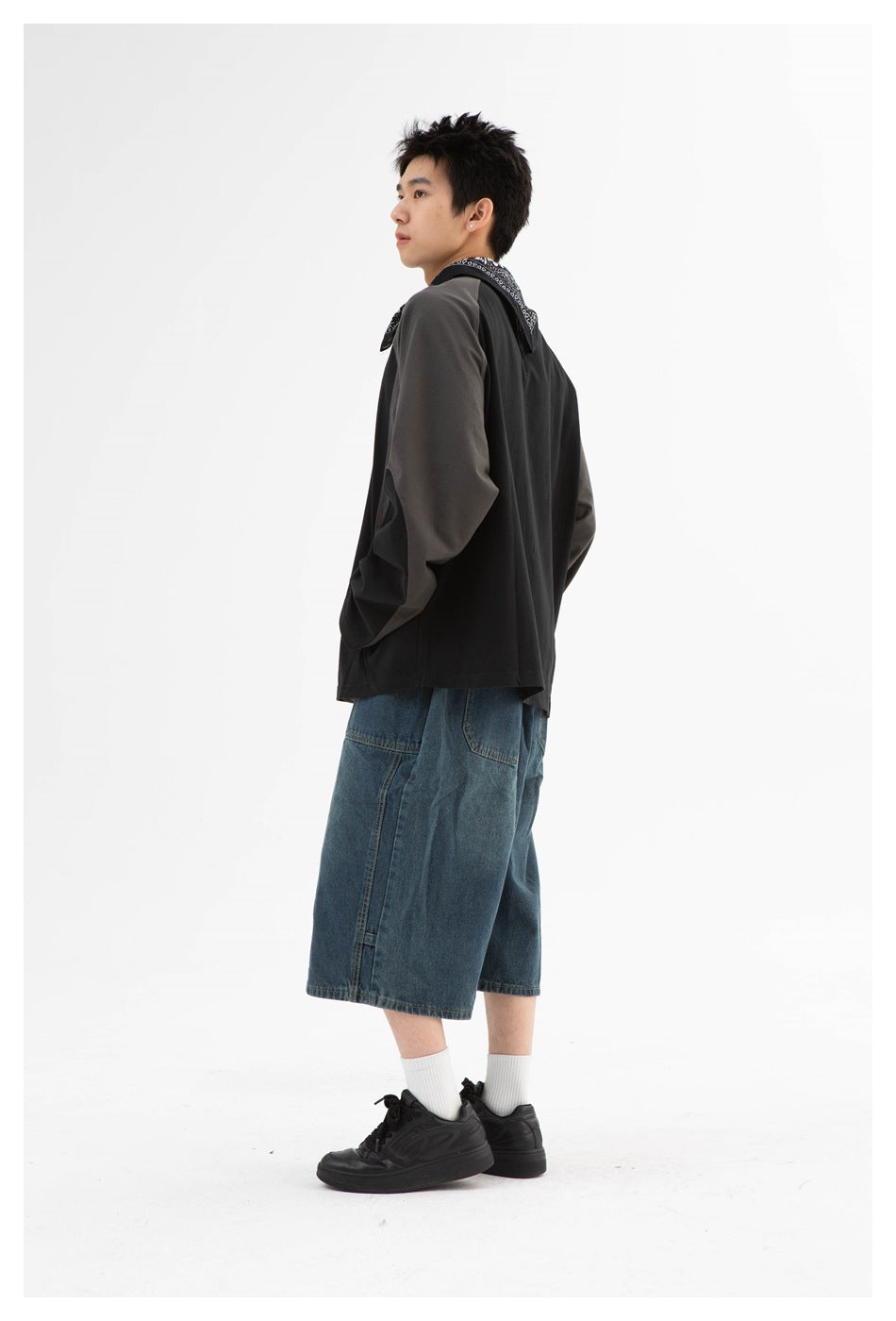 Side view of a model wearing a black sweatshirt with charcoal sleeves and loose blue denim shorts.