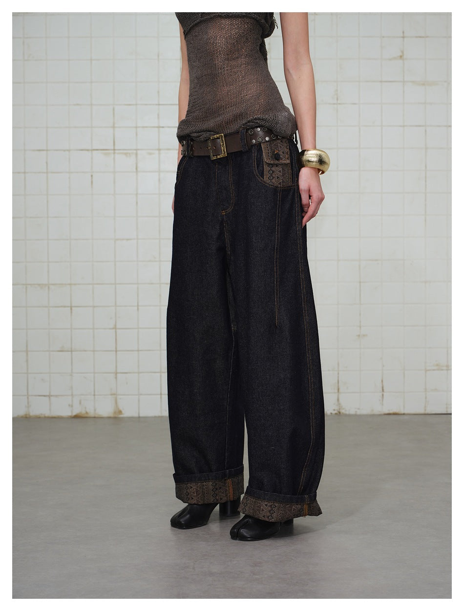 Front view of a person wearing dark barrel-leg jeans with patterned pocket panel, cuffed hems and a brown belt