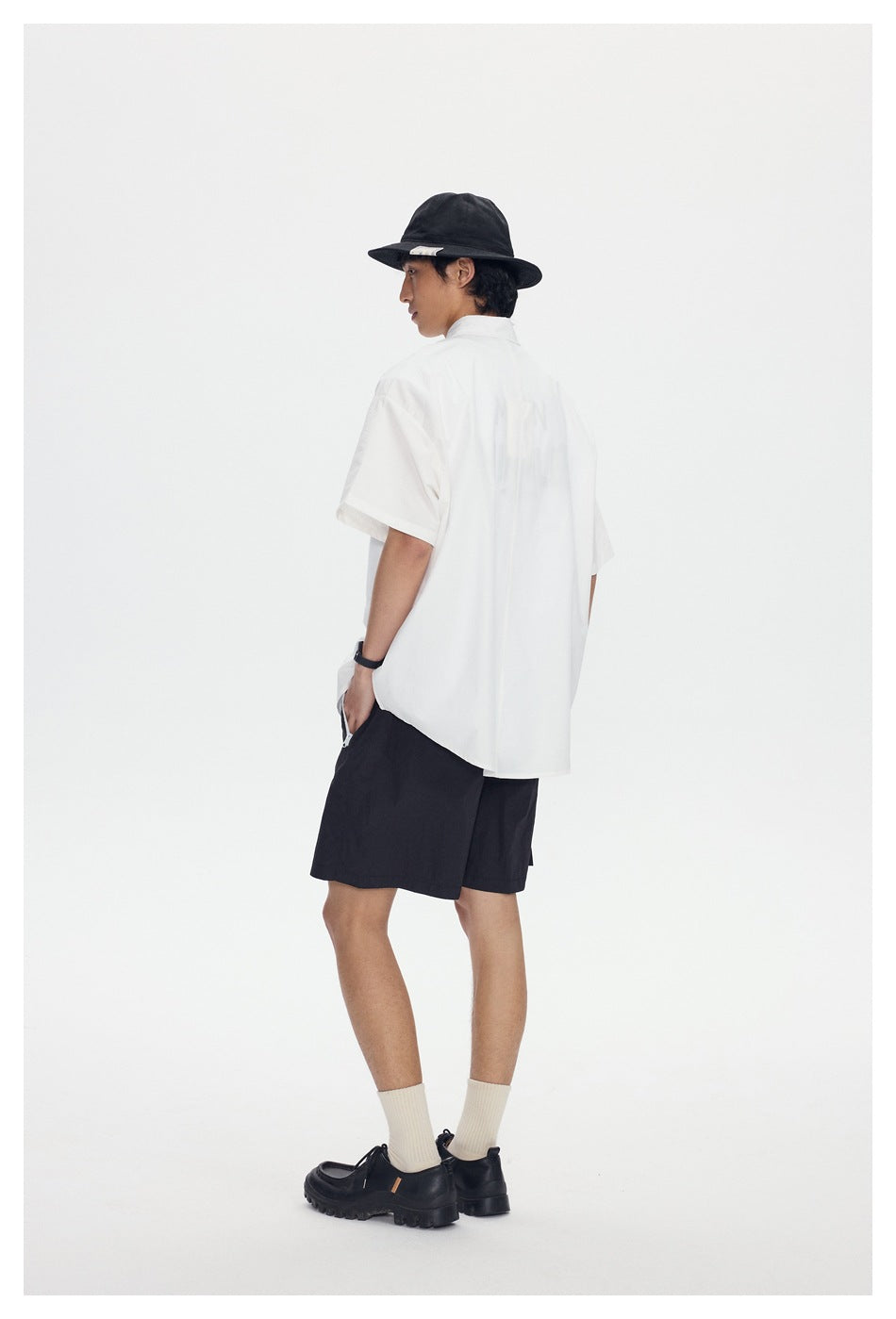 Rear view of a model wearing a white short-sleeve shirt and black shorts with a black hat.