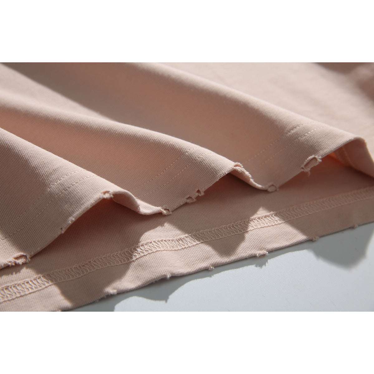 Close-up of the pale blush-pink T-shirt's raw, uneven hem and visible overlock stitching.