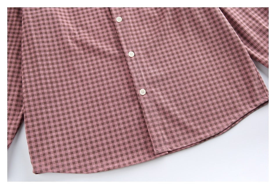 Lower front of a dusty pink and brown checked button-up shirt, with white buttons and a curved hem.