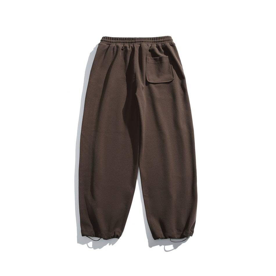 Dark brown relaxed-fit pants with an elastic drawstring waist, one patch pocket, and gathered ankle cuffs, shown flat.