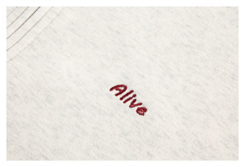 Close-up of red “alive” embroidery on off-white heathered fabric.