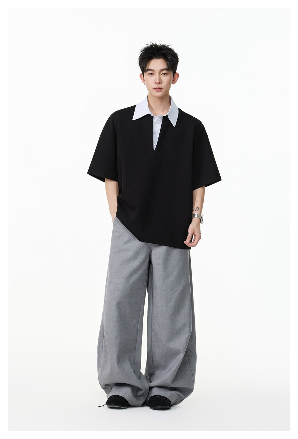 Model in a black short-sleeve polo-style top with a striped collar, worn with wide-leg gray trousers, full-length view