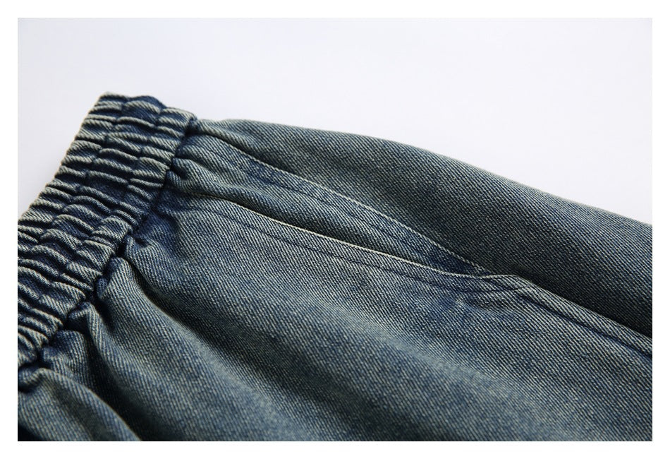 Close-up of a stitched pocket opening beside the gathered waistband on blue denim pants.