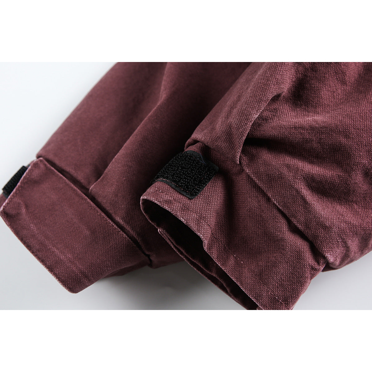 Close-up of a burgundy jacket cuff with a black hook-and-loop adjustment tab.