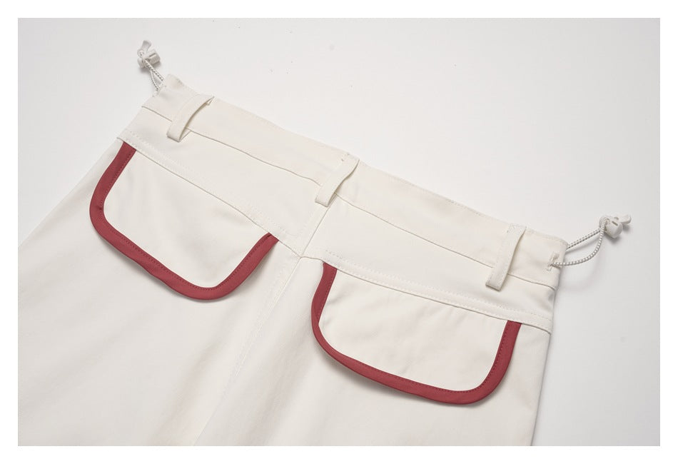 Close-up of a cream garment's waistband and two front pockets with muted red trim.