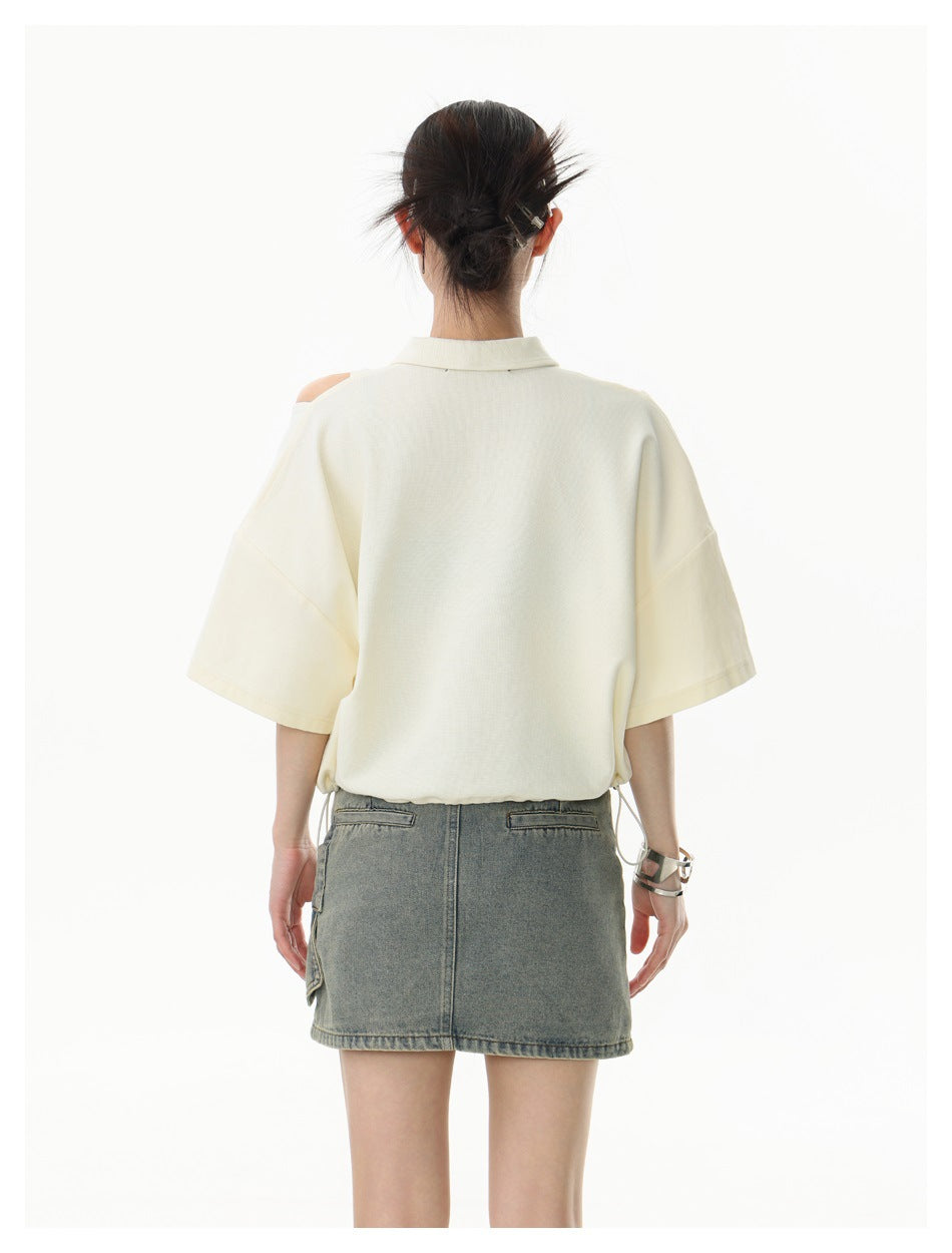Back view of a model wearing an ivory oversized short-sleeve collared top with a shoulder cutout and a gray denim skirt.