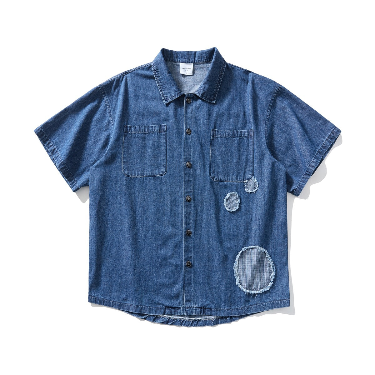 Dark blue washed denim short-sleeve button-up shirt with chest pockets and three round frayed patches, flat lay