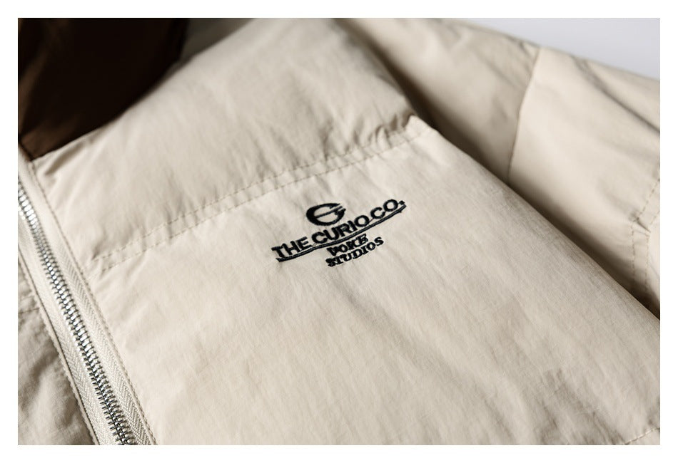 Close-up of black embroidered lettering on the chest of a cream jacket beside its silver zipper.