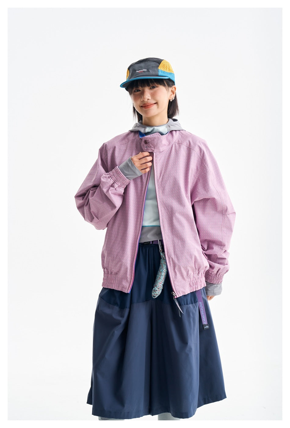 Closer front view of a model in a pink patterned zip jacket and navy skirt.