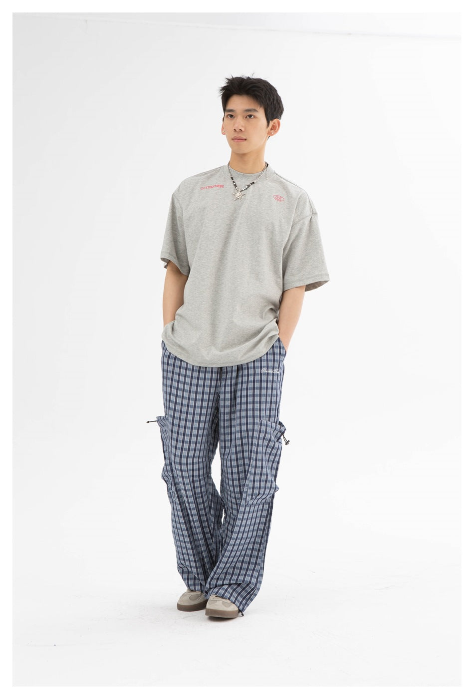 Model wearing blue plaid wide-leg pants with thigh pockets, a gray t-shirt and beige sneakers, standing full length
