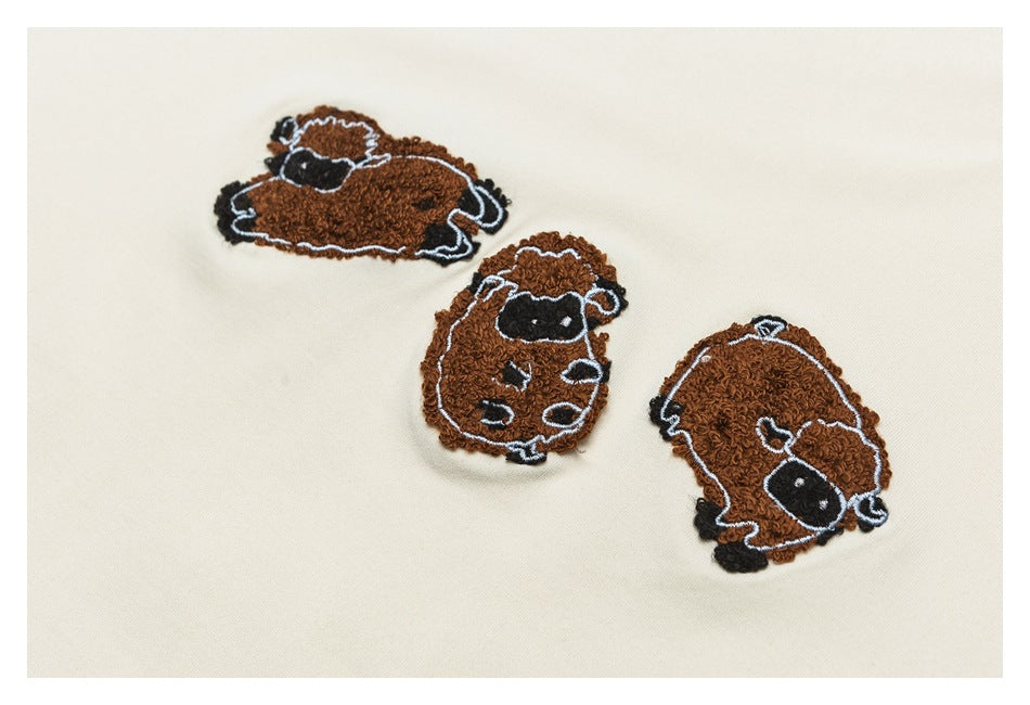 Three brown sheep embroidery designs on ivory sweatshirt fabric, shown in a cropped detail.