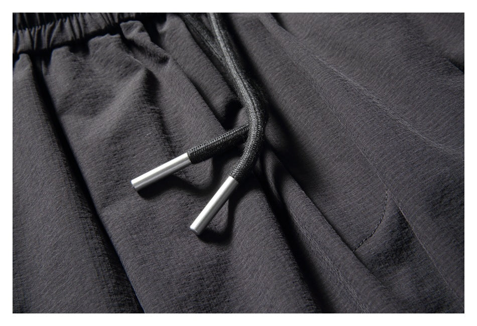 Close-up of charcoal pants with black drawstrings and silver-colored tips at the waistband.