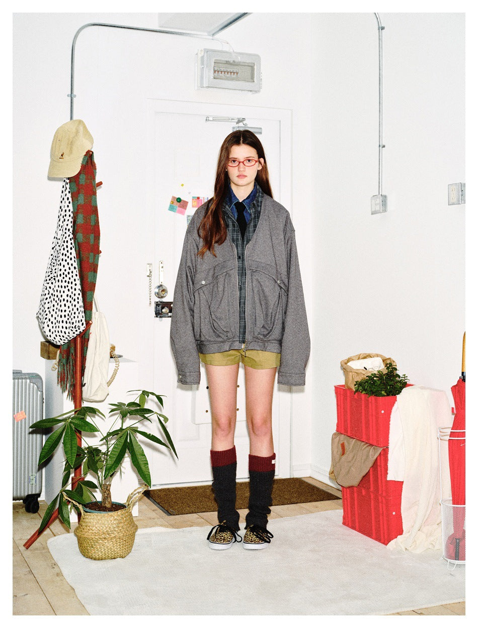 Front view of a model wearing an oversized gray zip jacket with large flap pockets and plaid layers underneath.