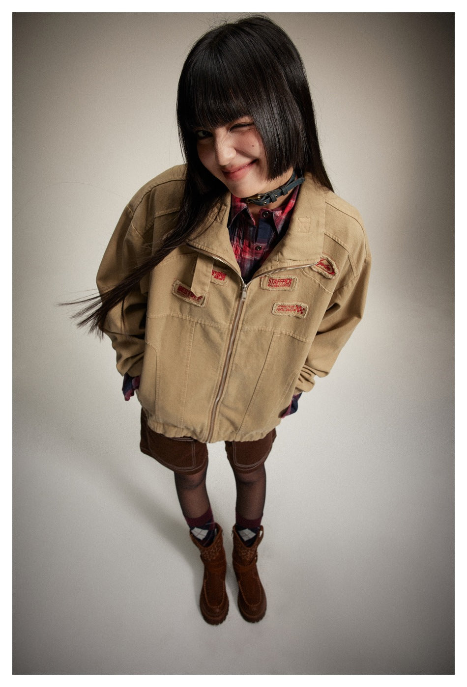Overhead view of a model wearing the tan patch-decorated jacket, red plaid shirt, and dark shorts.