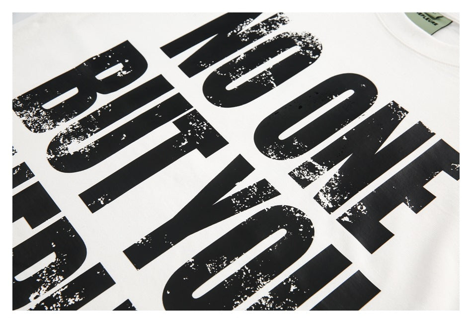 Angled close-up of distressed black lettering printed across a white T-shirt.