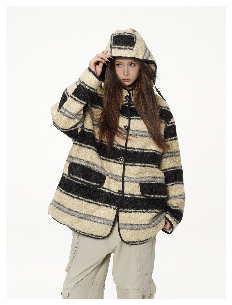 Model in an oversized striped hooded jacket with one hand raised to the hood, showing flap pockets and black piping